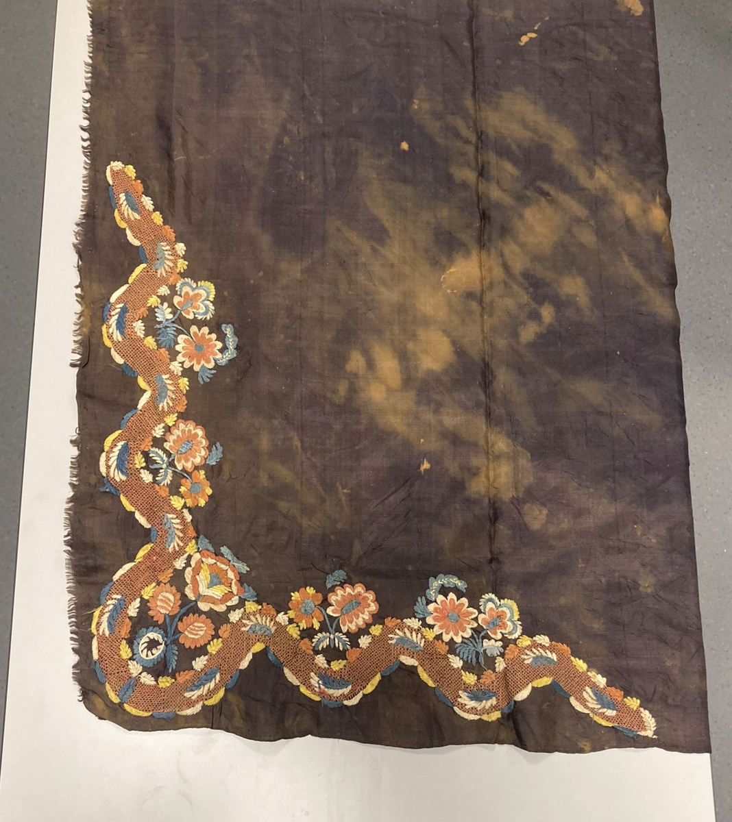Kvadratisk svart silketørkle. Brodert blomsterdekor i et hjørne. Falmet og blekeflekker, en frynset kant.