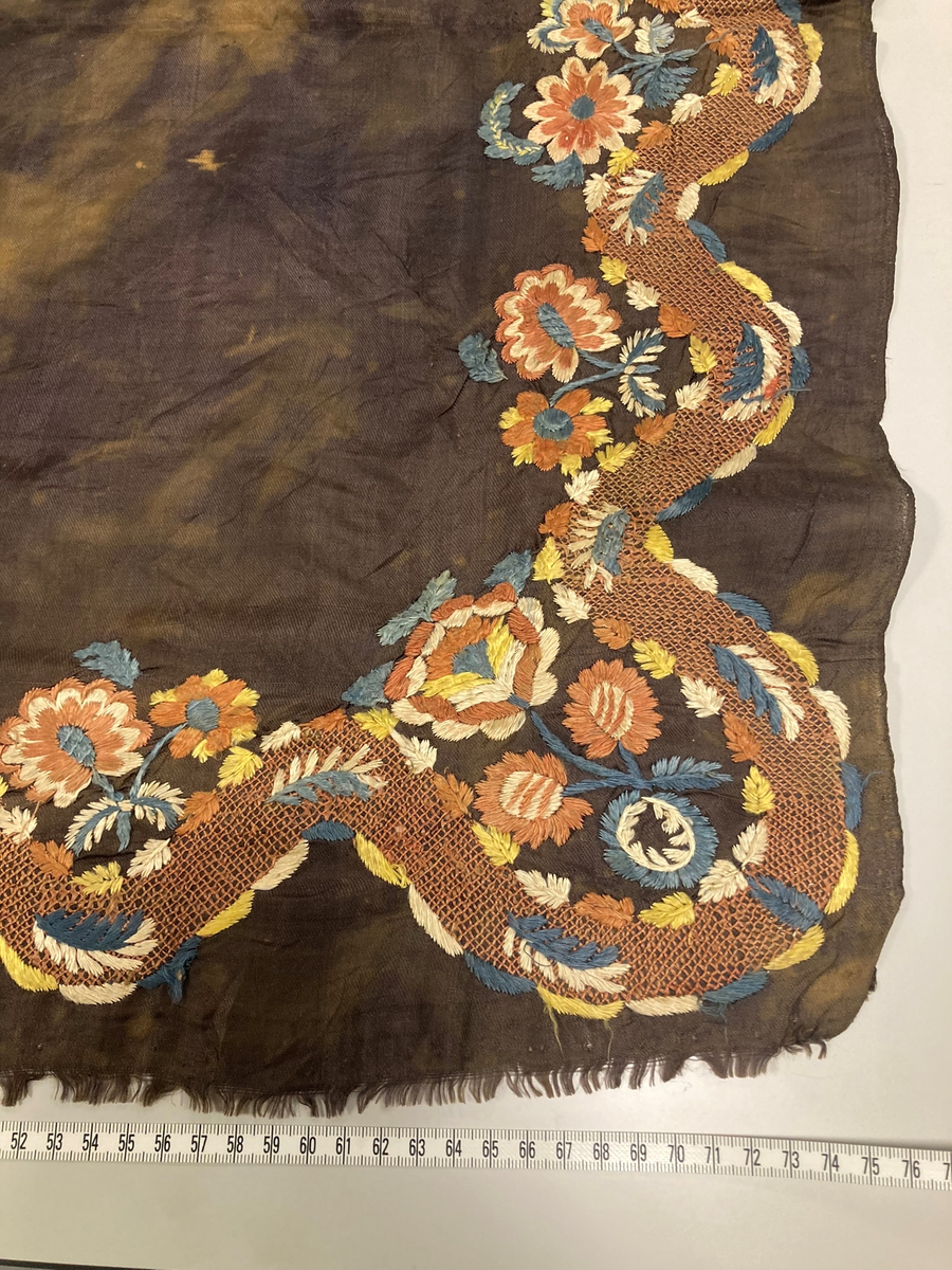 Kvadratisk svart silketørkle. Brodert blomsterdekor i et hjørne. Falmet og blekeflekker, en frynset kant.