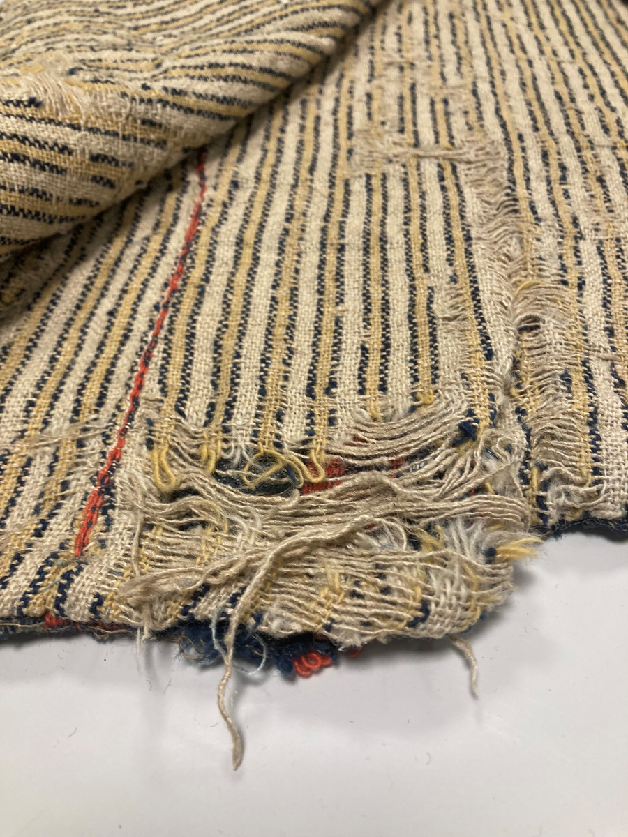 Ullvest med krage til mann i blått, grønt, rødt og hvitt. Dobbeltspent med tinnknapper. Foret med linstoff med gule/blå striper.