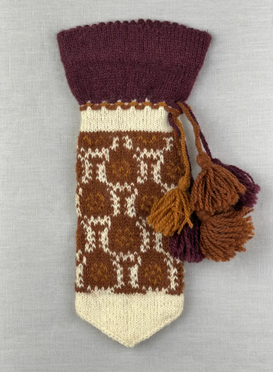 En stickad tumvante, med ett uddvarv vid fållvikning på krage och mönsterstickad vante i slätstickning, av 2-trådigt ullgarn. Vid handleden är 3 stycken finger-påtade snoddar inträdda. Varje snodd är avslutad med en tofs i vardera ände.

