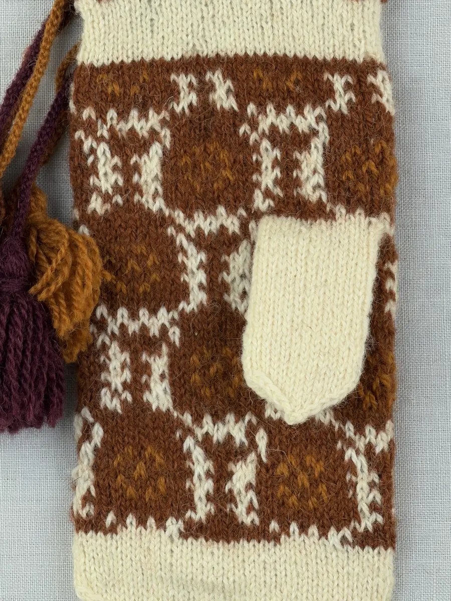 En stickad tumvante, med ett uddvarv vid fållvikning på krage och mönsterstickad vante i slätstickning, av 2-trådigt ullgarn. Vid handleden är 3 stycken finger-påtade snoddar inträdda. Varje snodd är avslutad med en tofs i vardera ände.

