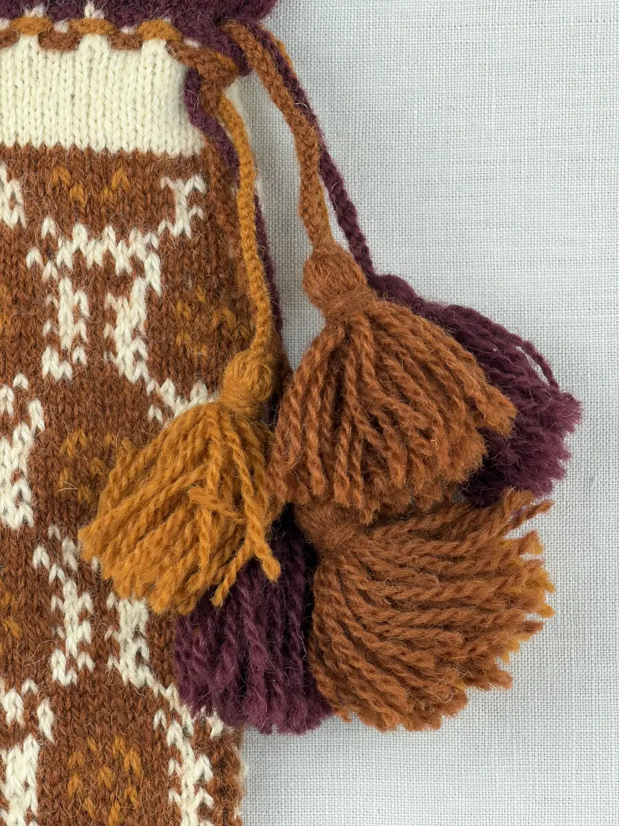 En stickad tumvante, med ett uddvarv vid fållvikning på krage och mönsterstickad vante i slätstickning, av 2-trådigt ullgarn. Vid handleden är 3 stycken finger-påtade snoddar inträdda. Varje snodd är avslutad med en tofs i vardera ände.

