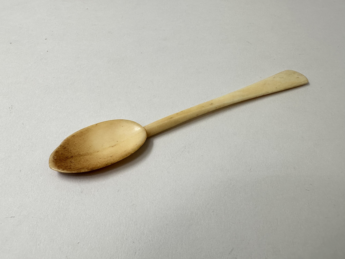 Äggsked av ben. Droppformat grunt blad, skaftet platt och utsväng mot änden, konvext skuret avslut. Missfärgat blad. 