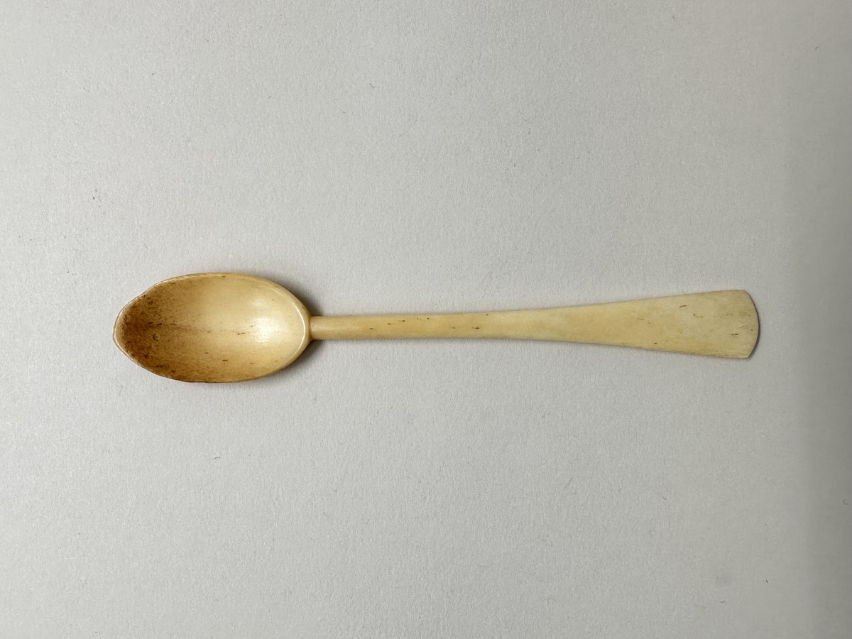 Äggsked av ben. Droppformat grunt blad, skaftet platt och utsväng mot änden, konvext skuret avslut. Missfärgat blad. 