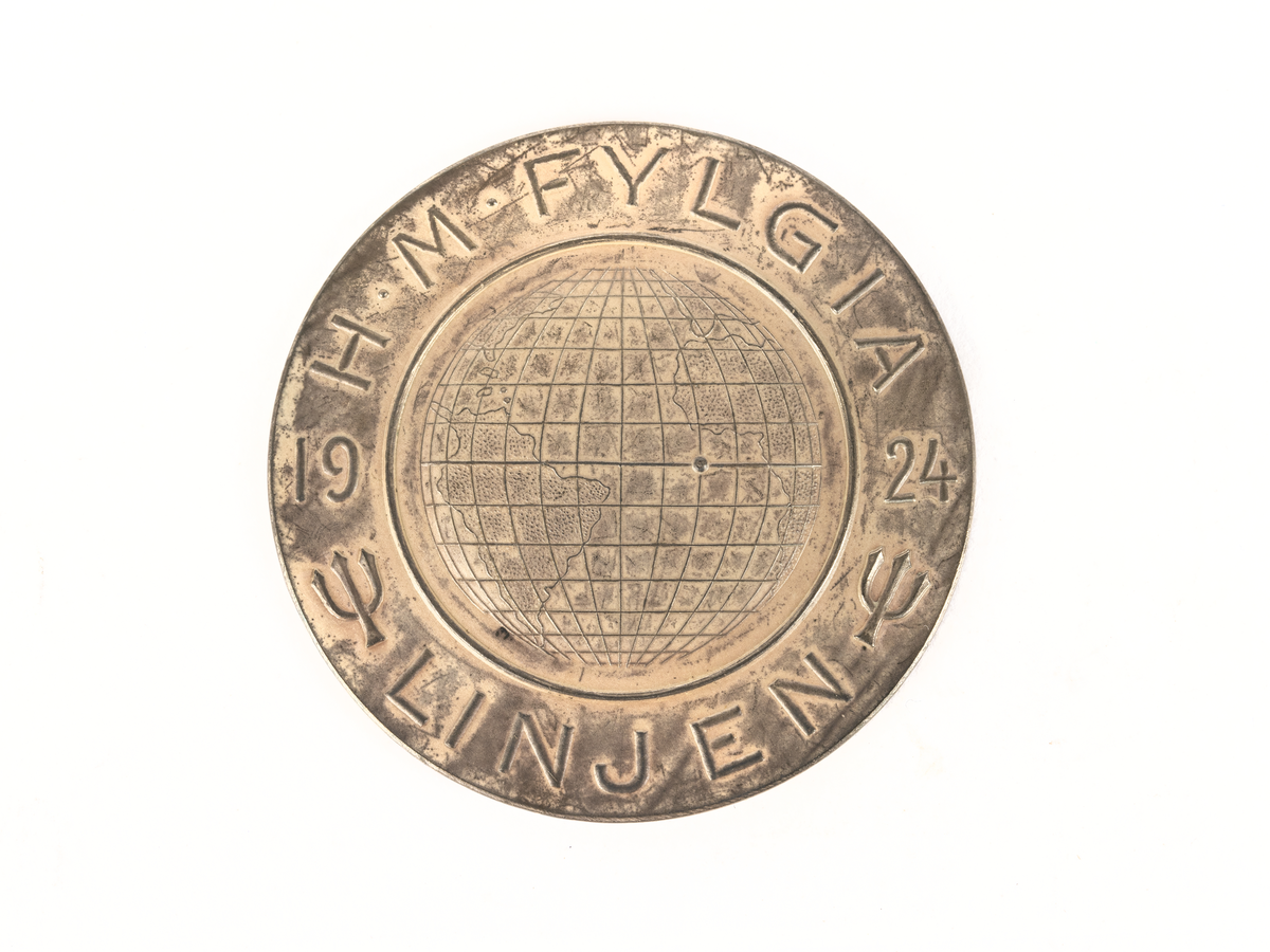 Åtsida: Bild av jordglob med platsmarkering på ekvatorn. Omgiven av 2 treuddar samt text: H.M. FYLGIA 1924 Linjen.
Frånsida: Bild av treudd och text: 19-27/12-24, lat. 0Â° o'o. W 6Â° 40'. Plats för gravering under.