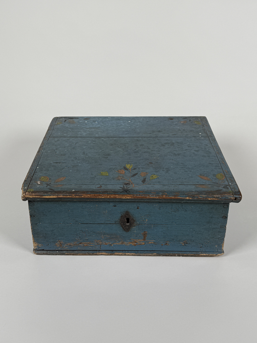 Skrin av furu med sinkade hörn och underifrån itappad botten. Gångjärn, låshake och nyckelskylt. Lås saknas (har varit utanpåliggande). Läddika med lock. Målat utvändigt med stiliserad blomsterdekor i gult, rött och svart mot heltäckande blå botten. 