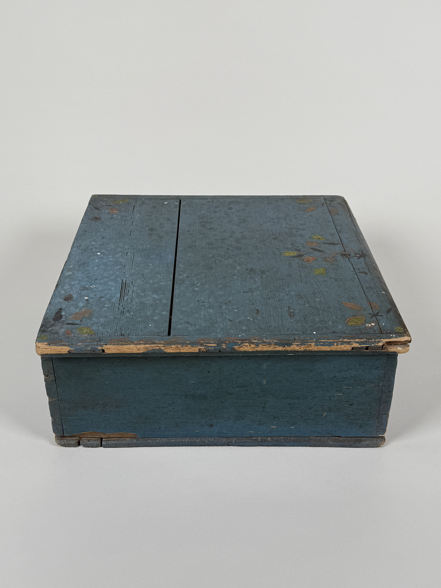 Skrin av furu med sinkade hörn och underifrån itappad botten. Gångjärn, låshake och nyckelskylt. Lås saknas (har varit utanpåliggande). Läddika med lock. Målat utvändigt med stiliserad blomsterdekor i gult, rött och svart mot heltäckande blå botten. 