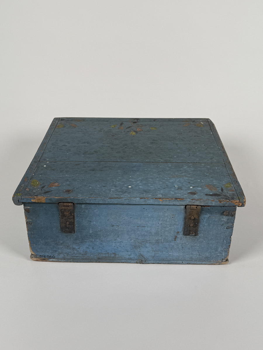 Skrin av furu med sinkade hörn och underifrån itappad botten. Gångjärn, låshake och nyckelskylt. Lås saknas (har varit utanpåliggande). Läddika med lock. Målat utvändigt med stiliserad blomsterdekor i gult, rött och svart mot heltäckande blå botten. 