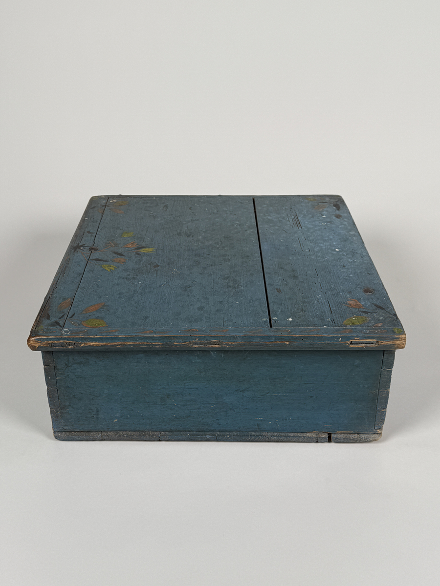 Skrin av furu med sinkade hörn och underifrån itappad botten. Gångjärn, låshake och nyckelskylt. Lås saknas (har varit utanpåliggande). Läddika med lock. Målat utvändigt med stiliserad blomsterdekor i gult, rött och svart mot heltäckande blå botten. 