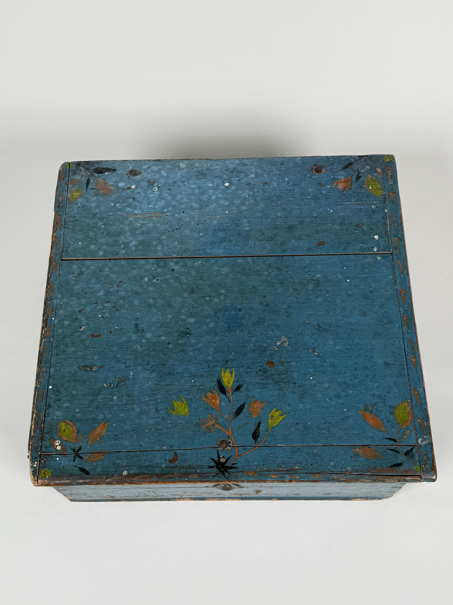 Skrin av furu med sinkade hörn och underifrån itappad botten. Gångjärn, låshake och nyckelskylt. Lås saknas (har varit utanpåliggande). Läddika med lock. Målat utvändigt med stiliserad blomsterdekor i gult, rött och svart mot heltäckande blå botten. 