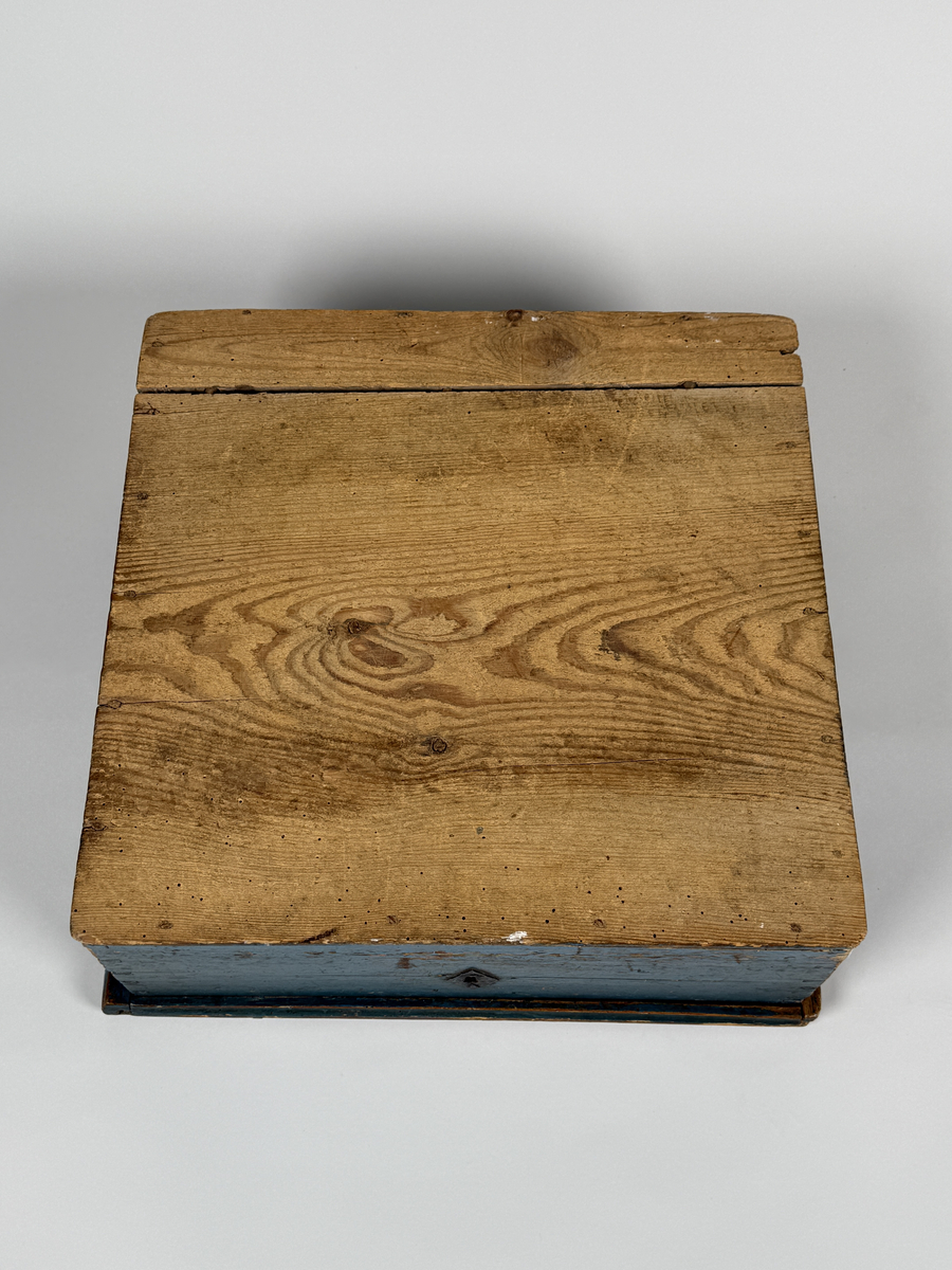 Skrin av furu med sinkade hörn och underifrån itappad botten. Gångjärn, låshake och nyckelskylt. Lås saknas (har varit utanpåliggande). Läddika med lock. Målat utvändigt med stiliserad blomsterdekor i gult, rött och svart mot heltäckande blå botten. 