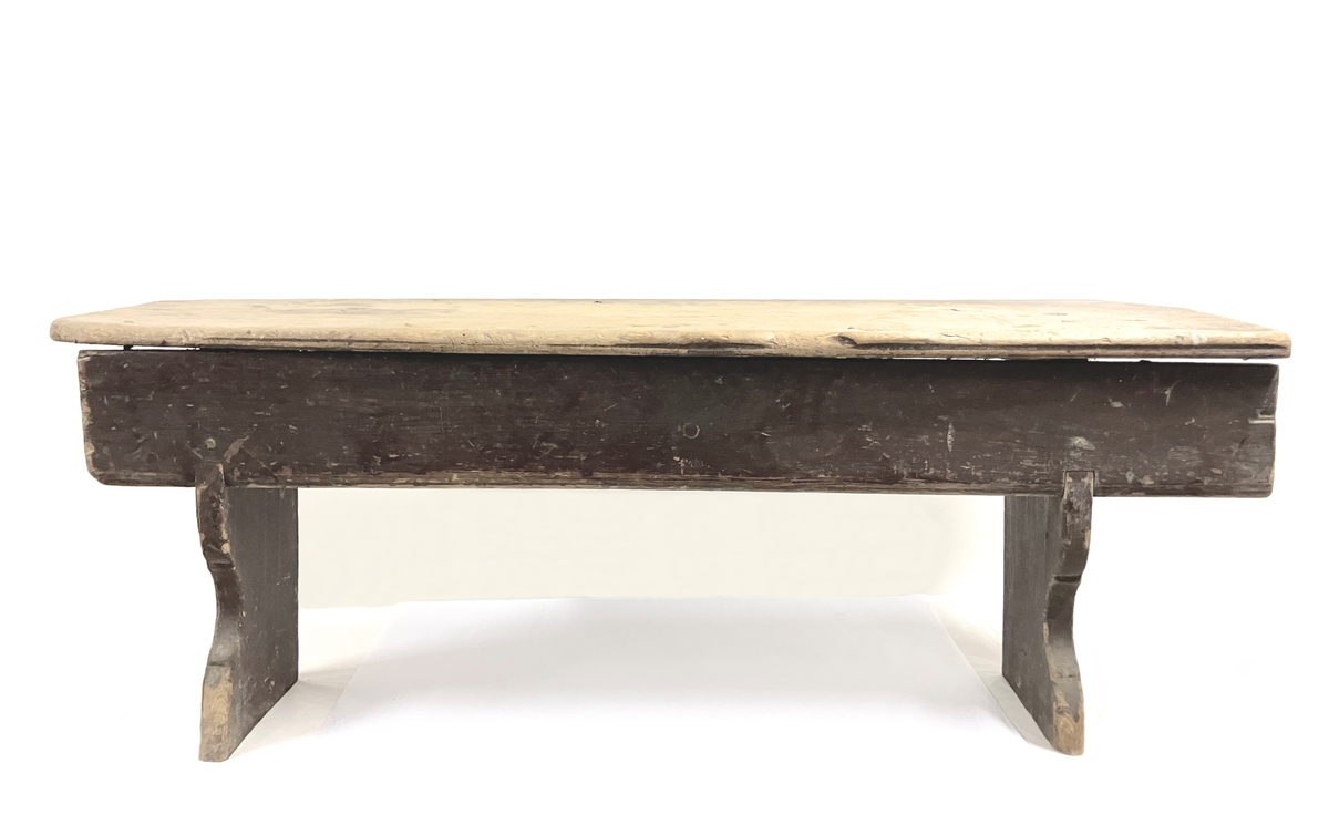 Målselv: Lundberg: Klasrommet: Husmannsplass: Benk: sittebenk: bygget opp av 2 tverr-tre, som er skåret med buer, som bærer en sitteplate. På ene siden et sidebord opp under toppbordet som låser konstruksjonen. Malt rødbrun. Sitteflaten nedslitt.