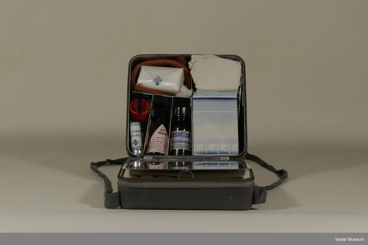 ERRO (Rolf Bølling & Co.) Førstehjelpsveske. Førstehjelps veske har et innebygget speil og inneholder :

Bang and Tegner & Co.(B&T&Co.) Sterilisert GAS x 4, Enkeltmannspakke x 2, Gasbind 5m x 6cm x1, Gasbind 5m x10cm x 2,  Triangelbind (Esmarchs tørkle u.fig) til bandasjering og et Stypisk Bomull glass.

Norges Plaster 2cm x 1m boks av Norges Plaster A/S.
(N.Sp.nr 1999 kat.no.002 Mosby og Skøyen). 
Norges Plaster 1m2 cont.ca.170g.
Massa Emplastica: Zinci Oxydun 20%, Massa Elastica 80%)

S.S.S N.P Steel Safety Pins, Made in England. S.S.S Steel Pins x 12.

LYSAKER APOTEK, LYSAKER. Jod Bensin glasset : Meget ildsfarlig!
Obs! Må holdes tett tilluket da væsken gjør luften eksplosiv farlig, må den ikke bruke i nærheten av ild, bart lys eller elektriske apparater. (Tømt)

LYSAKER APOTEK; Kamferdråper. Til medinsinsk bruk 10 - 20 dråper ad gangen.

1 x Bandasje.

1 x sachet av PYRISEPT ... Innholdet løst i 1 liter vann gir Pyrisept. oppl. 10/00 Til sårrensing. PYRISEPT WEIFA.

Zik-Zak Renset Bomull 10g

Et lengde av en gummi røret.

1 x Øyebadeglass.

1x Pinsett.

1x Liten saks - Made in Germany.

1x Bruksanvisning/ reklame til ERRO (Rolf Bølling & Co.) 

1x Faktura fra ERRO (Rolf Bølling & Co.) datert 29.Okt 1957 tilsendte til Vardølotteforbund v/ Aud Paulsen. (se. bilde no.7)