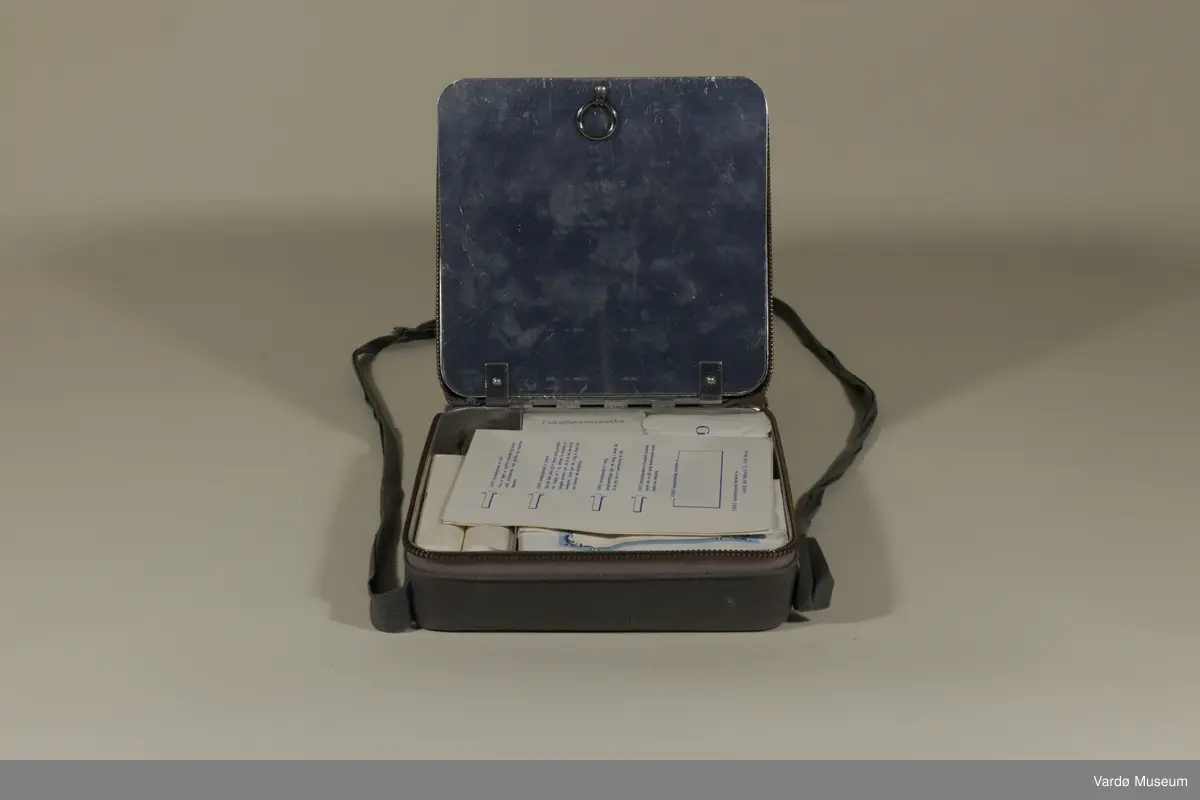 ERRO (Rolf Bølling & Co.) Førstehjelpsveske. Førstehjelps veske har et innebygget speil og inneholder :

Bang and Tegner & Co.(B&T&Co.) Sterilisert GAS x 4, Enkeltmannspakke x 2, Gasbind 5m x 6cm x1, Gasbind 5m x10cm x 2,  Triangelbind (Esmarchs tørkle u.fig) til bandasjering og et Stypisk Bomull glass.

Norges Plaster 2cm x 1m boks av Norges Plaster A/S.
(N.Sp.nr 1999 kat.no.002 Mosby og Skøyen). 
Norges Plaster 1m2 cont.ca.170g.
Massa Emplastica: Zinci Oxydun 20%, Massa Elastica 80%)

S.S.S N.P Steel Safety Pins, Made in England. S.S.S Steel Pins x 12.

LYSAKER APOTEK, LYSAKER. Jod Bensin glasset : Meget ildsfarlig!
Obs! Må holdes tett tilluket da væsken gjør luften eksplosiv farlig, må den ikke bruke i nærheten av ild, bart lys eller elektriske apparater. (Tømt)

LYSAKER APOTEK; Kamferdråper. Til medinsinsk bruk 10 - 20 dråper ad gangen.

1 x Bandasje.

1 x sachet av PYRISEPT ... Innholdet løst i 1 liter vann gir Pyrisept. oppl. 10/00 Til sårrensing. PYRISEPT WEIFA.

Zik-Zak Renset Bomull 10g

Et lengde av en gummi røret.

1 x Øyebadeglass.

1x Pinsett.

1x Liten saks - Made in Germany.

1x Bruksanvisning/ reklame til ERRO (Rolf Bølling & Co.) 

1x Faktura fra ERRO (Rolf Bølling & Co.) datert 29.Okt 1957 tilsendte til Vardølotteforbund v/ Aud Paulsen. (se. bilde no.7)