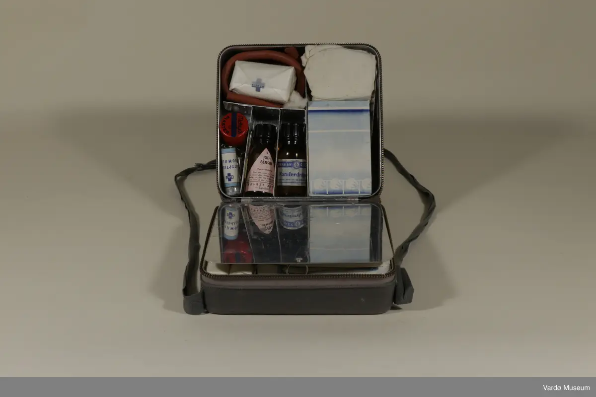 ERRO (Rolf Bølling & Co.) Førstehjelpsveske. Førstehjelps veske har et innebygget speil og inneholder :

Bang and Tegner & Co.(B&T&Co.) Sterilisert GAS x 4, Enkeltmannspakke x 2, Gasbind 5m x 6cm x1, Gasbind 5m x10cm x 2,  Triangelbind (Esmarchs tørkle u.fig) til bandasjering og et Stypisk Bomull glass.

Norges Plaster 2cm x 1m boks av Norges Plaster A/S.
(N.Sp.nr 1999 kat.no.002 Mosby og Skøyen). 
Norges Plaster 1m2 cont.ca.170g.
Massa Emplastica: Zinci Oxydun 20%, Massa Elastica 80%)

S.S.S N.P Steel Safety Pins, Made in England. S.S.S Steel Pins x 12.

LYSAKER APOTEK, LYSAKER. Jod Bensin glasset : Meget ildsfarlig!
Obs! Må holdes tett tilluket da væsken gjør luften eksplosiv farlig, må den ikke bruke i nærheten av ild, bart lys eller elektriske apparater. (Tømt)

LYSAKER APOTEK; Kamferdråper. Til medinsinsk bruk 10 - 20 dråper ad gangen.

1 x Bandasje.

1 x sachet av PYRISEPT ... Innholdet løst i 1 liter vann gir Pyrisept. oppl. 10/00 Til sårrensing. PYRISEPT WEIFA.

Zik-Zak Renset Bomull 10g

Et lengde av en gummi røret.

1 x Øyebadeglass.

1x Pinsett.

1x Liten saks - Made in Germany.

1x Bruksanvisning/ reklame til ERRO (Rolf Bølling & Co.) 

1x Faktura fra ERRO (Rolf Bølling & Co.) datert 29.Okt 1957 tilsendte til Vardølotteforbund v/ Aud Paulsen. (se. bilde no.7)