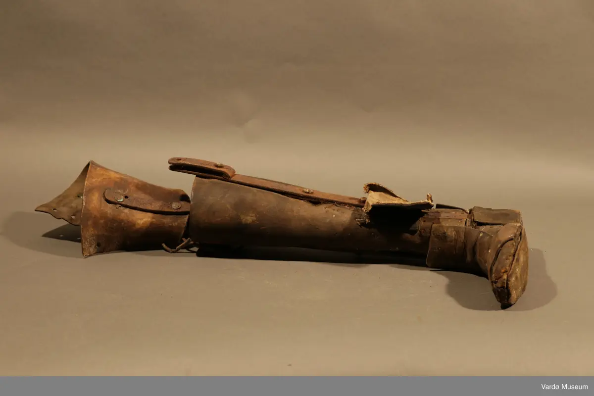 Benprotese . Gjenstand er kledd i rødbrunt lær på legg, fot og lår. Protesen har fire hull på øverste del til både stramme og løsne av et snørebånd.