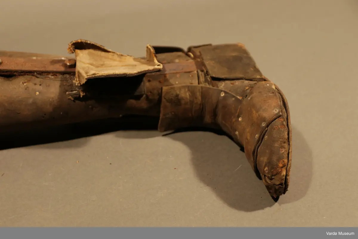 Benprotese . Gjenstand er kledd i rødbrunt lær på legg, fot og lår. Protesen har fire hull på øverste del til både stramme og løsne av et snørebånd.