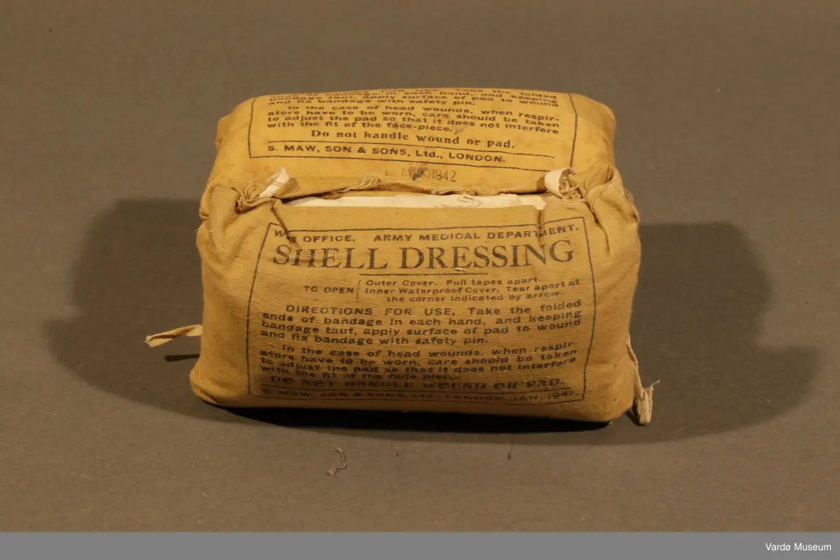 39 Kompress/Bandasje (Shell Dressing)  av flere forskjellige produsent, og med flere forskjellige produksjons datoer påskrevet på pakninger. Rektangulær lerret pose med knytting. Inn i posen er det kompress i bomull, på utsiden er det trykket tekst.