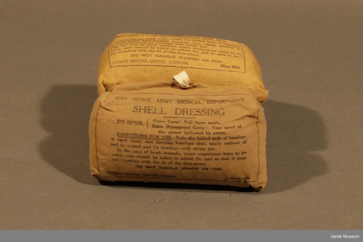 39 Kompress/Bandasje (Shell Dressing)  av flere forskjellige produsent, og med flere forskjellige produksjons datoer påskrevet på pakninger. Rektangulær lerret pose med knytting. Inn i posen er det kompress i bomull, på utsiden er det trykket tekst.