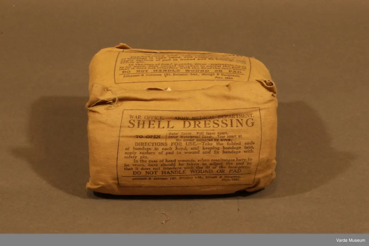 39 Kompress/Bandasje (Shell Dressing)  av flere forskjellige produsent, og med flere forskjellige produksjons datoer påskrevet på pakninger. Rektangulær lerret pose med knytting. Inn i posen er det kompress i bomull, på utsiden er det trykket tekst.