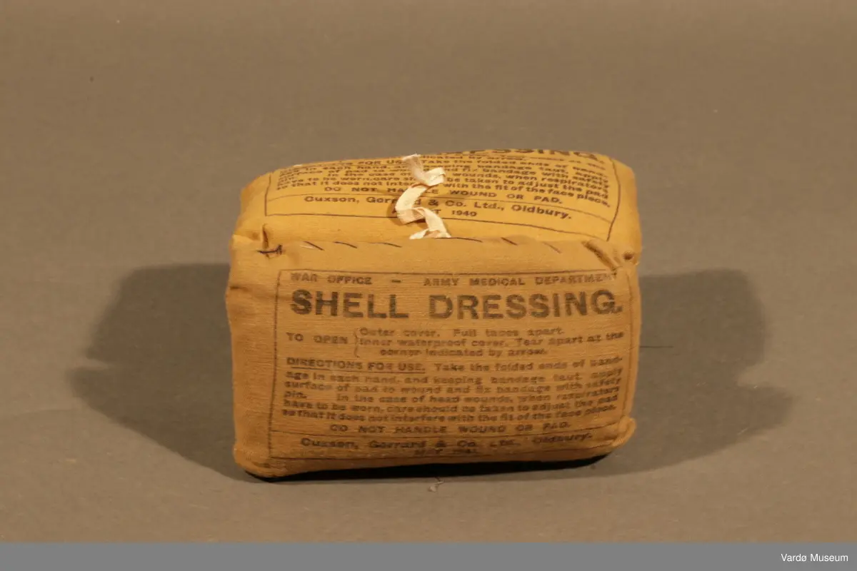 39 Kompress/Bandasje (Shell Dressing)  av flere forskjellige produsent, og med flere forskjellige produksjons datoer påskrevet på pakninger. Rektangulær lerret pose med knytting. Inn i posen er det kompress i bomull, på utsiden er det trykket tekst.