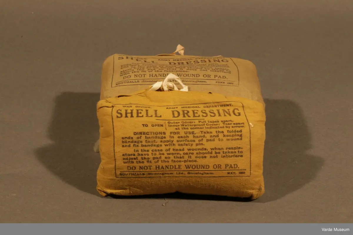 39 Kompress/Bandasje (Shell Dressing)  av flere forskjellige produsent, og med flere forskjellige produksjons datoer påskrevet på pakninger. Rektangulær lerret pose med knytting. Inn i posen er det kompress i bomull, på utsiden er det trykket tekst.