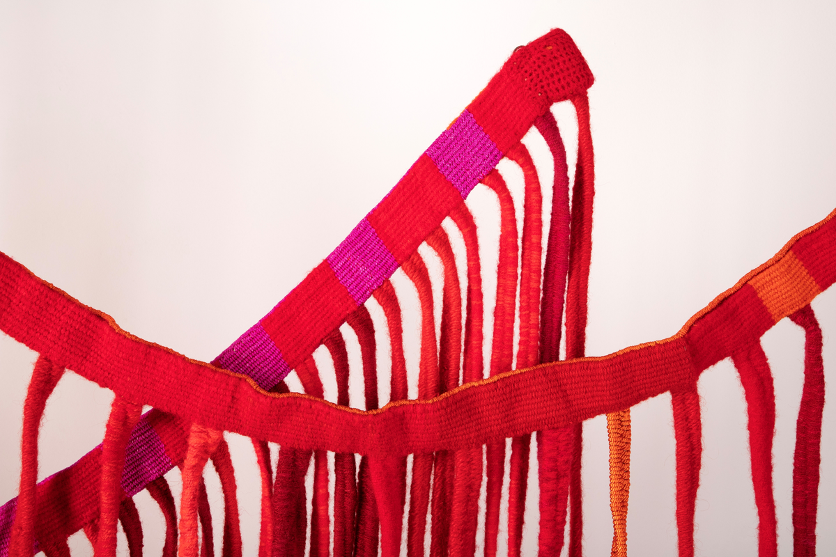 Tekstilskulptur i gobelinvev. Verket består av to lange vevde bånd. Fra disse båndene henger det ned lange, smale bånd. Materialene er kraftig, ufarget lingarn i renningen og kunstvevgarn, åklegarn og ryegarn i innslaget. Fargene på båndene er i en rødskala fra rødlilla, kald rød, varm rød til oransje.