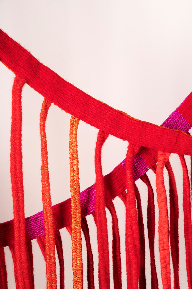 Tekstilskulptur i gobelinvev. Verket består av to lange vevde bånd. Fra disse båndene henger det ned lange, smale bånd. Materialene er kraftig, ufarget lingarn i renningen og kunstvevgarn, åklegarn og ryegarn i innslaget. Fargene på båndene er i en rødskala fra rødlilla, kald rød, varm rød til oransje.