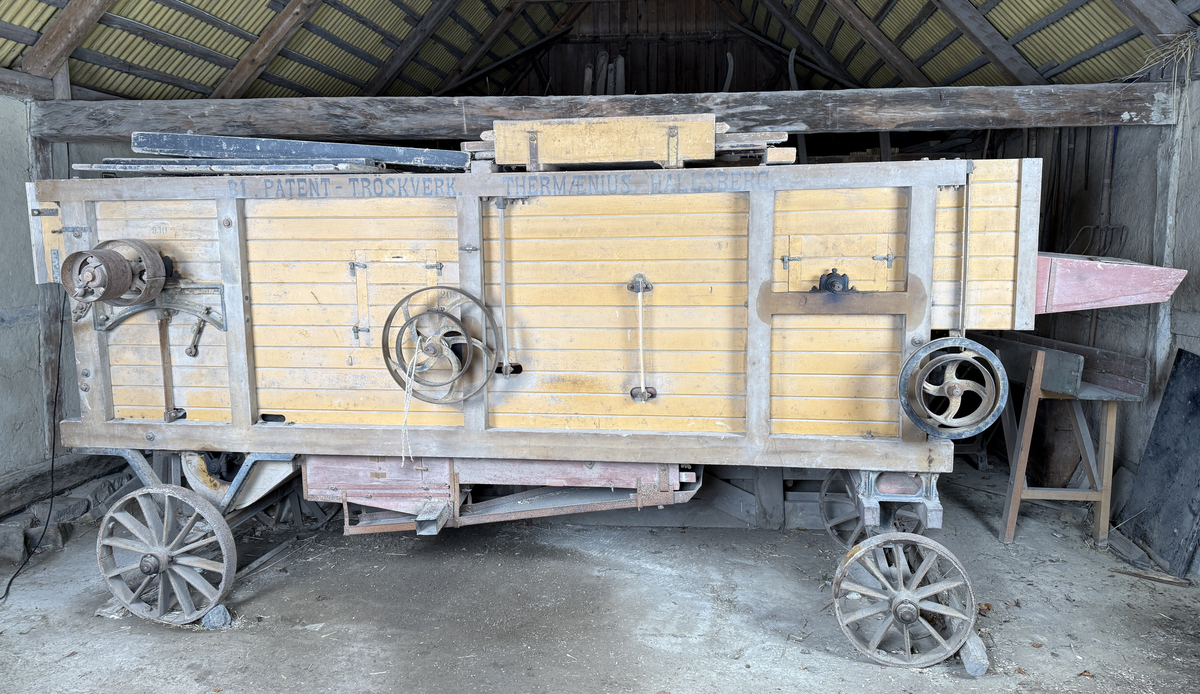 Tröskverk, fabriksgjort av AB Thermaeius & Sons, Hallsberg. Tillverkningsnummer 13 780. Avsett för drift med elmotor, tändkulemotor eller dragare, med remtransmission. Försålt av Generalförsäljare Kullberg & Co A.B. Katrineholm.
Verket består av en stor låda, byggd av trä och målad med gul färg. Det står på fyra hjul av gjutjärn. Inuti lådan finns ett maskineri av järn. Användandet tillgår så, att den torkade säden lastas in av en person i ena änden av lådan. Personen står på ett nerfällt flak och har ett matarbord till öppningen framför sig. Till vänster finns ett avtagbart bord, där kärven kan knytas upp. Kärven kommer först till en trumma av järn, där axen slås sönder. Trumman roterar med 950 v/min, enligt målad angivelse på utsidan. Där anges också rotationsriktningen. Även halmen trasas upp. Nertill i lådan finns en fläkt, som blåser undan bosset. De tunga sädeskornen faller ner i botten till en ränna, som leder till elevatorn. I denna, ett litet paternosterverk, lyfts säden upp för att sedan kunna falla ner i tre luckförsedda säckhållare. Halmen passerar ett skakverk och kommer ut i andra änden. 
Tranmissionsremmarna är av gummerad väv. Det går en rem från motorn till trummans axel. Dessutom går två drivremmar därifrån till skakverket, som har två funktioner: en för upp- och nergående rörelse, en för framåt-bakåtgående rörelse. På andra sidan finns drivremmar till fläkten och till elevatorn. Transmissionen skyddas av två enkla trägrindar. Utdraget mäter verket ungefär 5 580 mm. Största bredd med alla utbyggnader är 1 460 mm.
Stiften i trumman är sekundärt utbytta mot järnstift.
Under 1922 levererades 14 000 verk av denna typ, enkelrensande, transportabla och försedda med hjul. 

Funktion: Maskin som slår loss sädeskornen ur axen