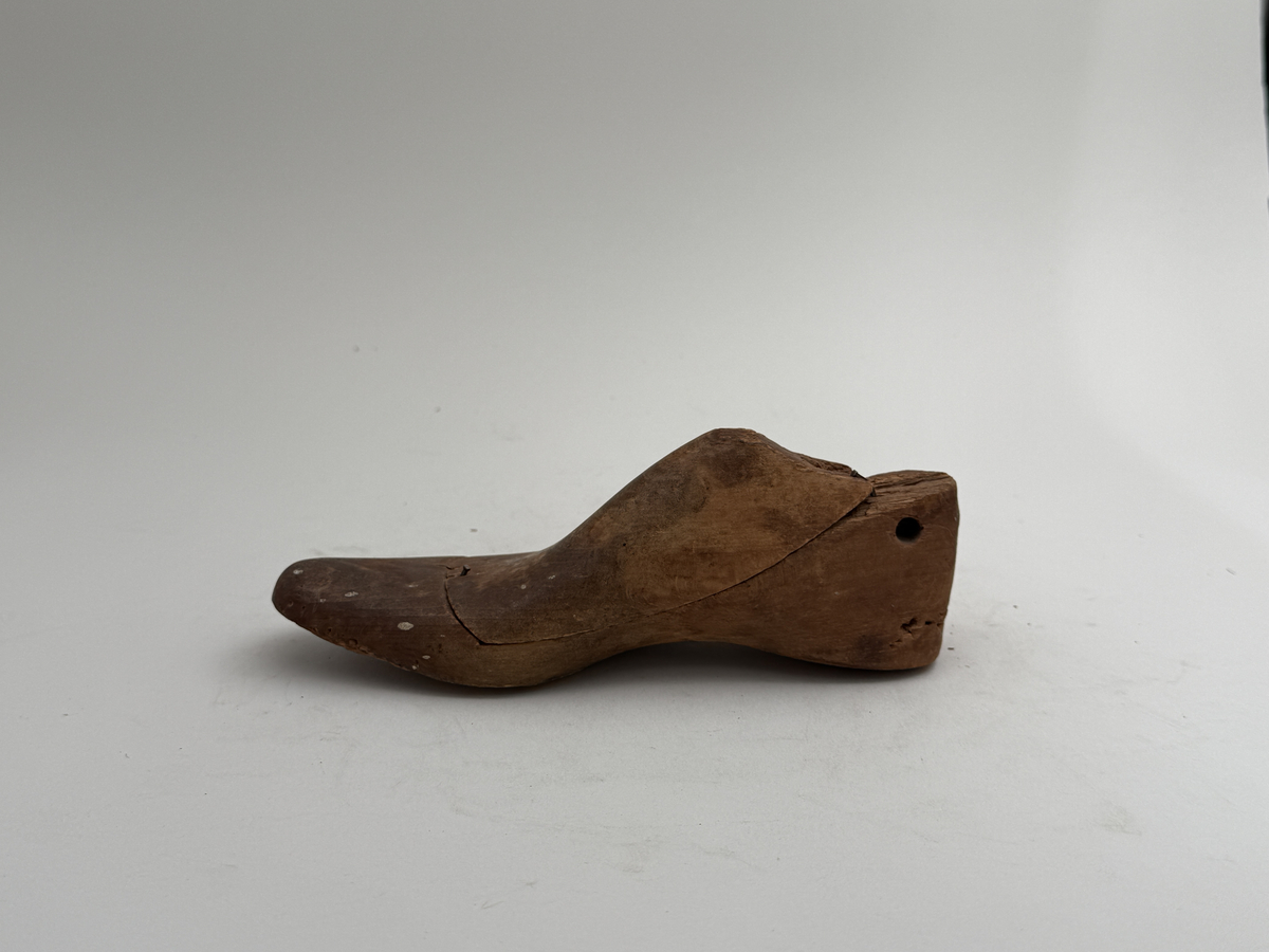 Skoläst, för högerfot, av bok. Överdelen lös. Hål för upphängning genom hälen.
 