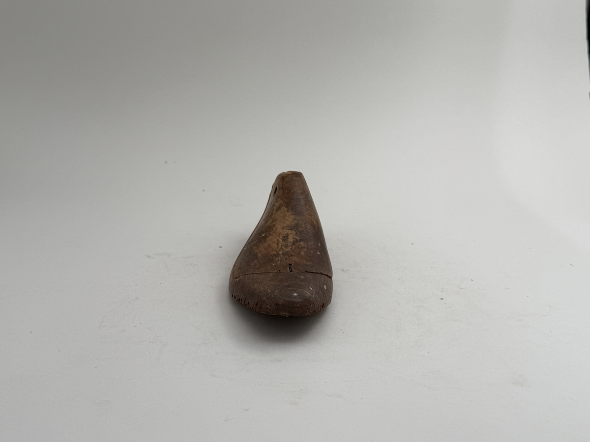 Skoläst, för högerfot, av bok. Överdelen lös. Hål för upphängning genom hälen.
 