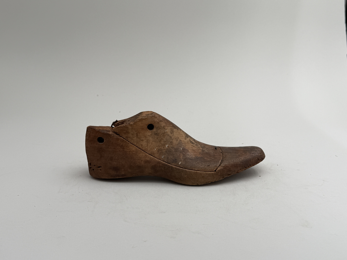 Skoläst, för högerfot, av bok. Överdelen lös. Hål för upphängning genom hälen.
 