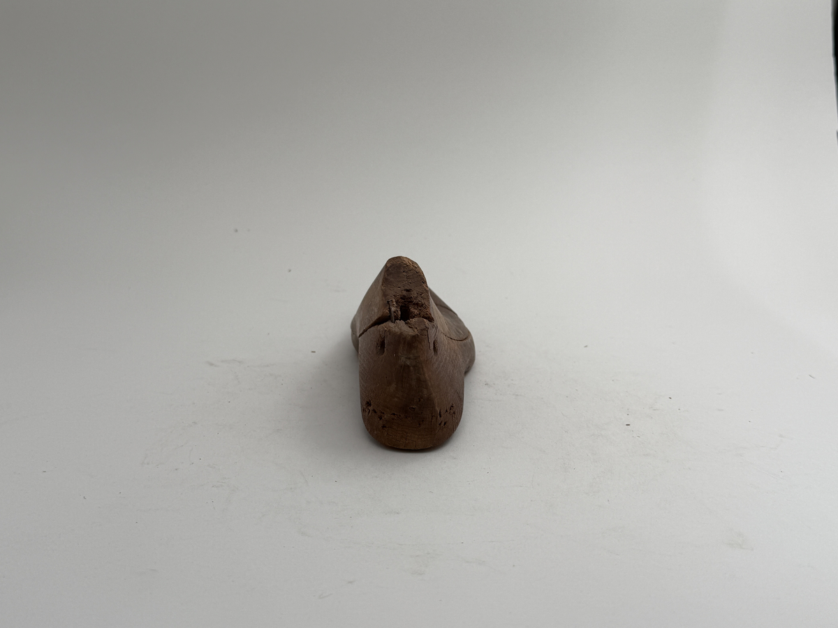 Skoläst, för högerfot, av bok. Överdelen lös. Hål för upphängning genom hälen.
 