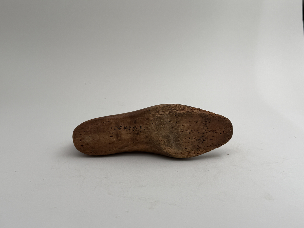 Skoläst, för högerfot, av bok. Överdelen lös. Hål för upphängning genom hälen.
 