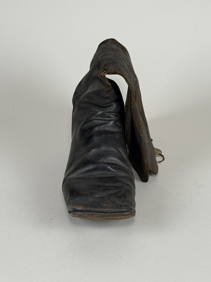 Stövel av svart läder, för höger fot, med rak tå, två dragstroppar av vävda band. Sula av läder. Skaften upptill fodrade med gulvitt skinn. 