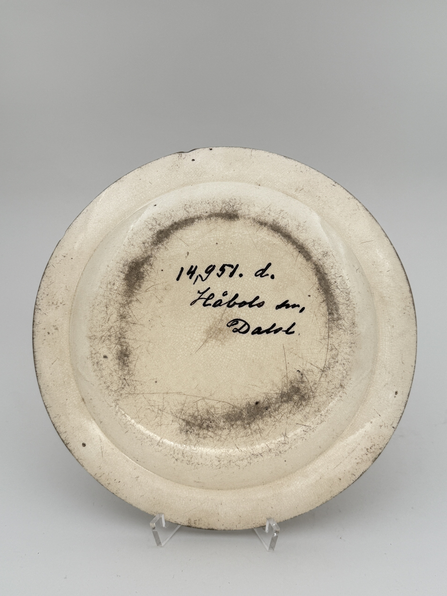 Flat tallrik av flintgods. Brämen dekorerad med två smala överglasyrmålade band i grönt. 