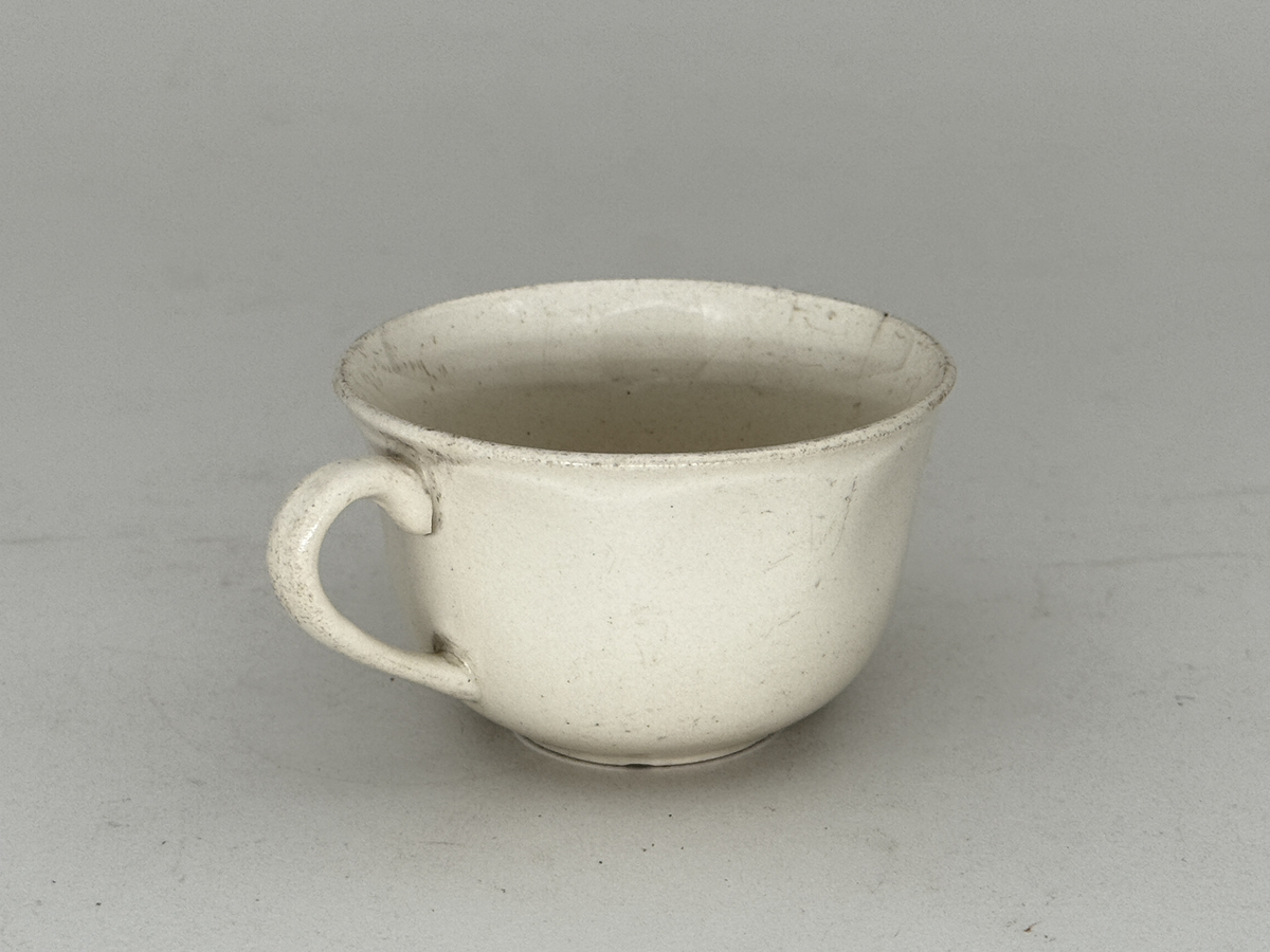 Kopp med öra,  lätt utsvängd kant, under kanten ett vågband i låd relief. 