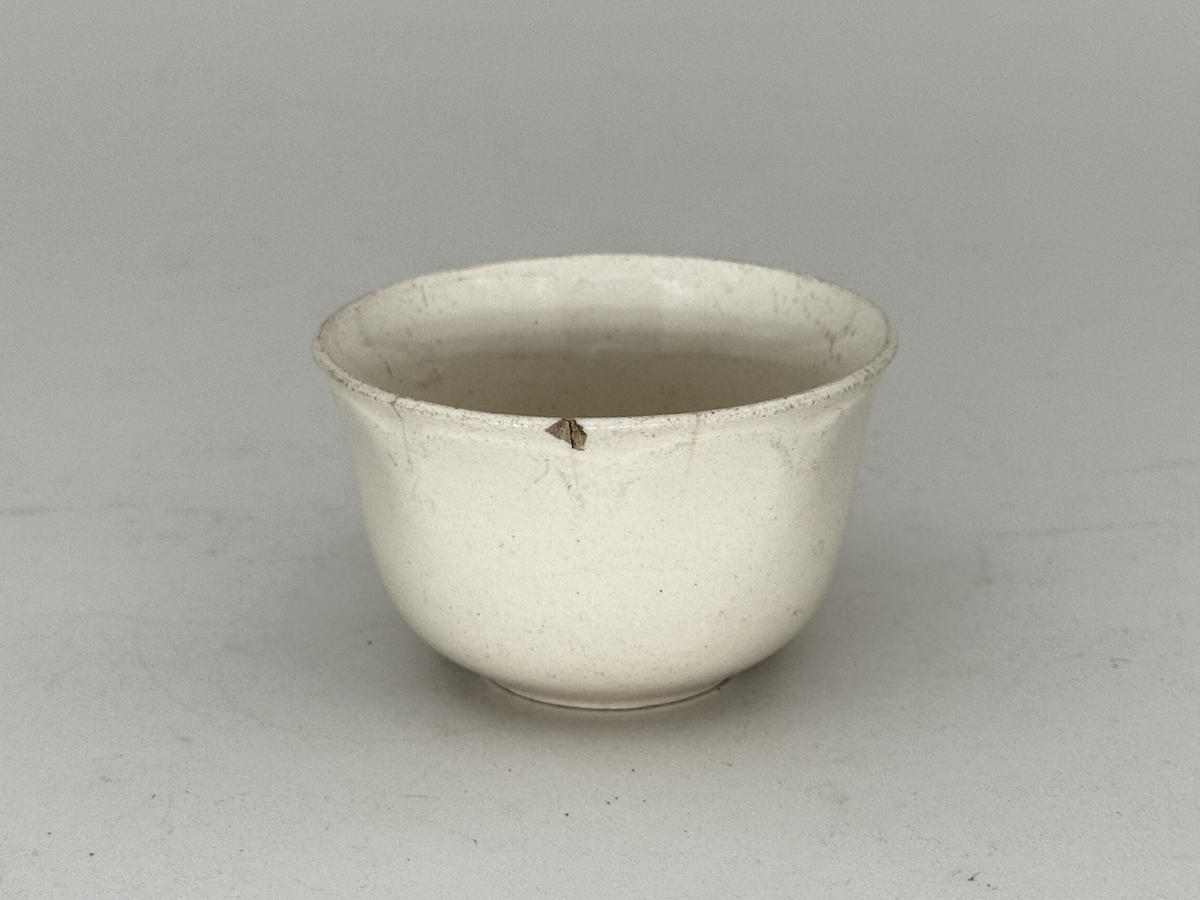 Kopp med öra,  lätt utsvängd kant, under kanten ett vågband i låd relief. 