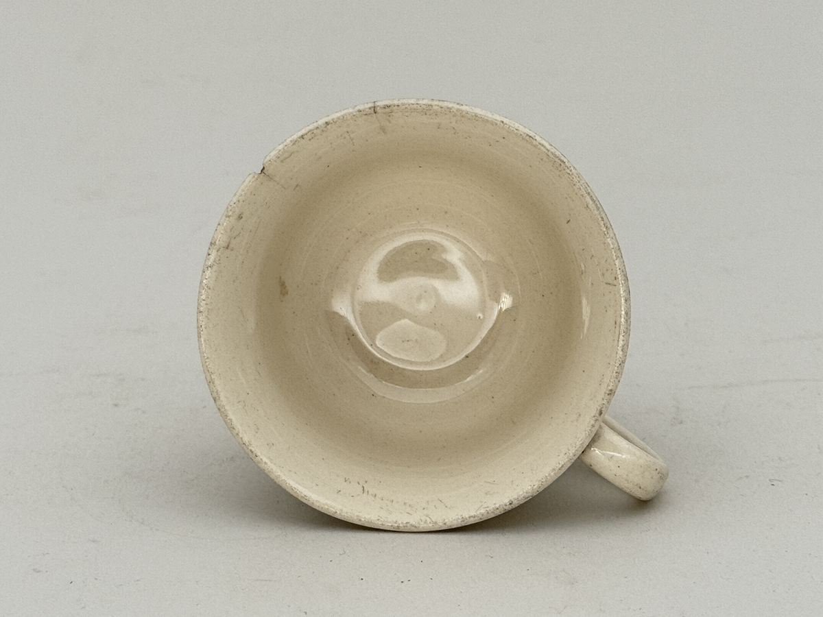 Kopp med öra,  lätt utsvängd kant, under kanten ett vågband i låd relief. 