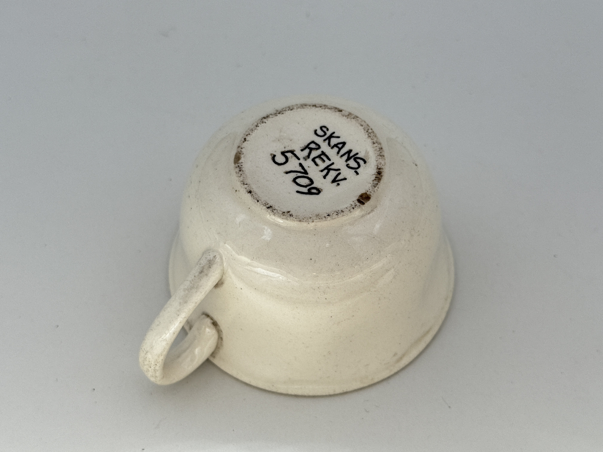 Kopp med öra,  lätt utsvängd kant, under kanten ett vågband i låd relief. 