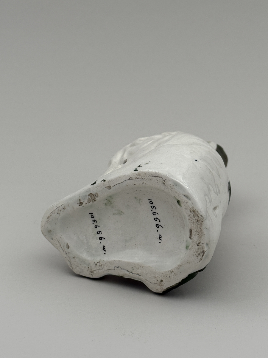 Figurin av porslin i form av sittande hund med halsband, glaserad, med överglasymålad dekor och förgyllning (förgyllningen mestadels bortnött).  
 