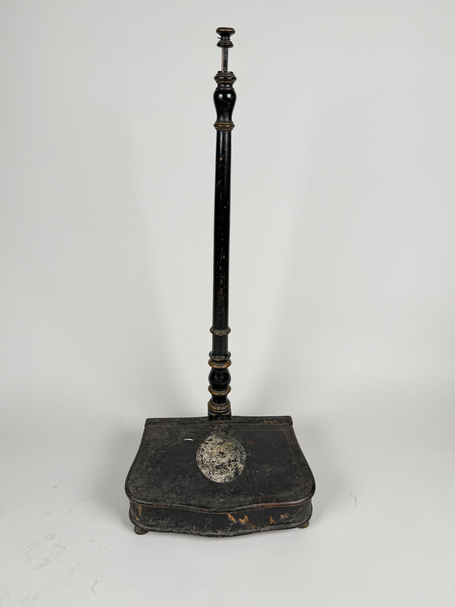 Spottlåda av svärtat trä, delvis fanerad, på kulfötter.  Lock med gångjärn, dekorerat med ljus medaljong. Profilsvarvat skaft fäst vid lådans bakre kant, mekanisk öppning genom att man trycker på knappen överst på skaftet. 