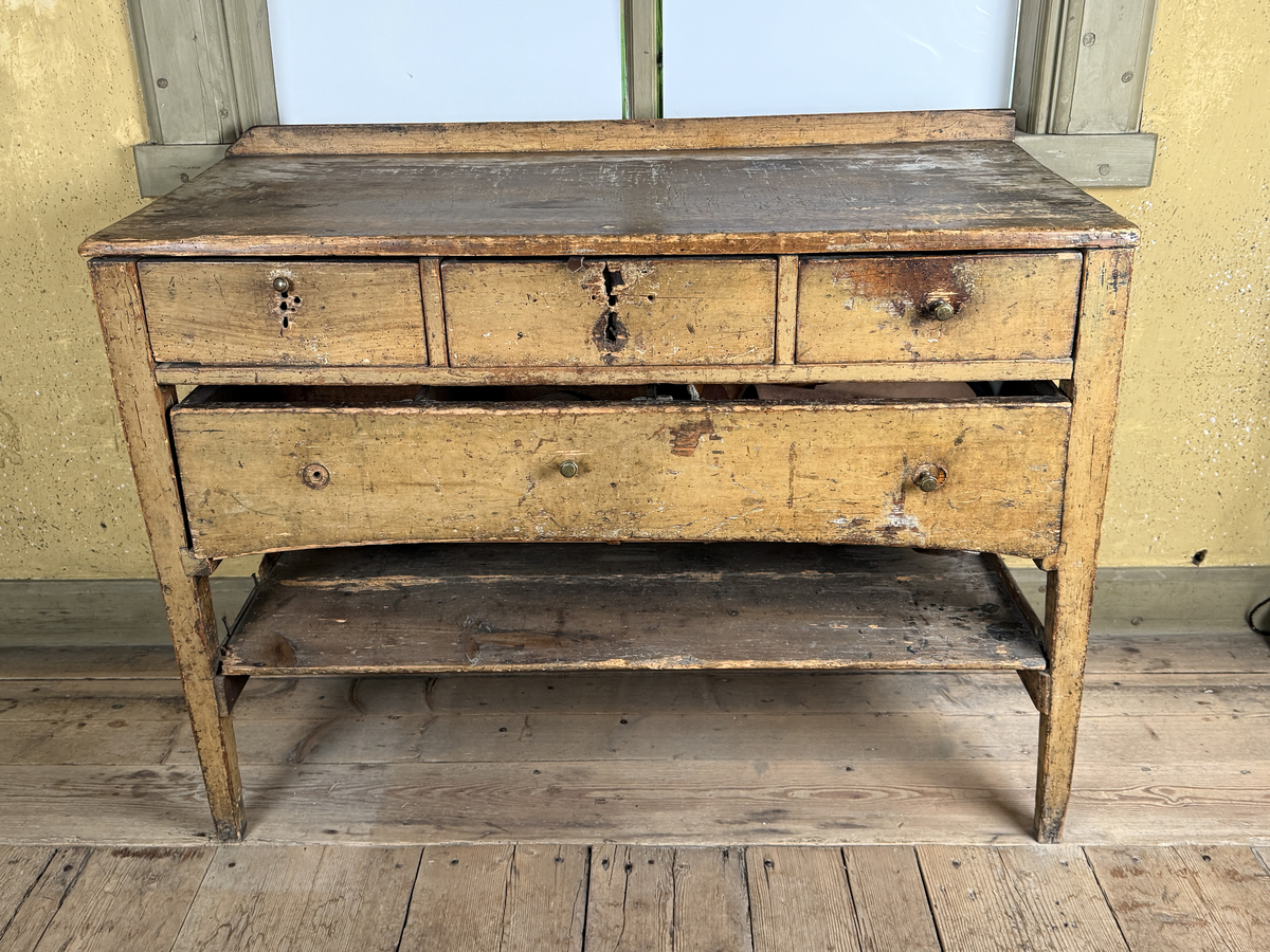 Avlastningsbord med rektangulär form, bemålad i beige-gult. Trågkant i skivans bakre kant. Övre lådvarvet med tre lådor, det undre lådvarvet med en låda. Längst ner en hylla. Dragknoppar av mässing, några saknas.