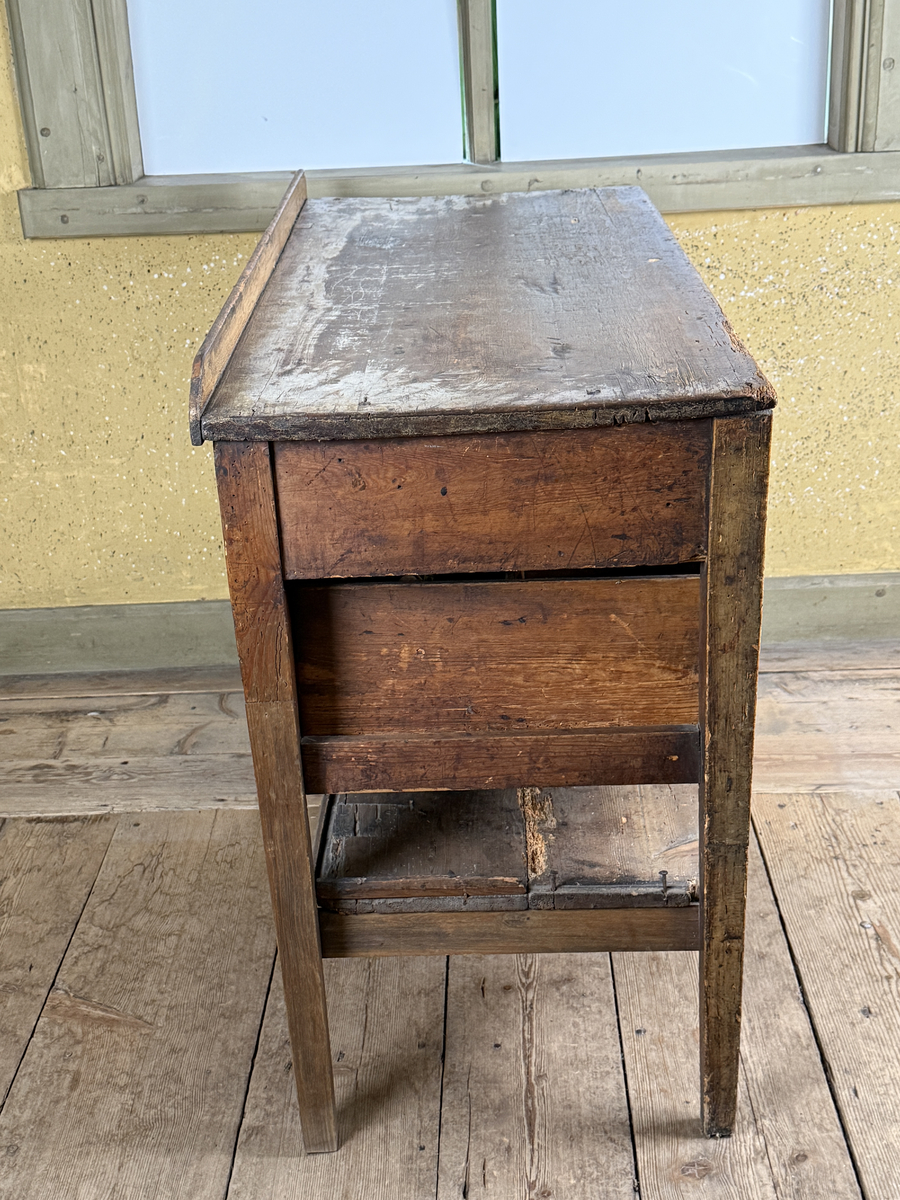 Avlastningsbord med rektangulär form, bemålad i beige-gult. Trågkant i skivans bakre kant. Övre lådvarvet med tre lådor, det undre lådvarvet med en låda. Längst ner en hylla. Dragknoppar av mässing, några saknas.