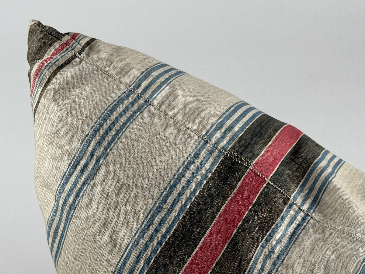 Rektangulär kudde av kypertvävd bomull, randig i svart, blått och rött. Förstärkta hörn. Stoppad med dun. Enstaka smärre lagningar. 