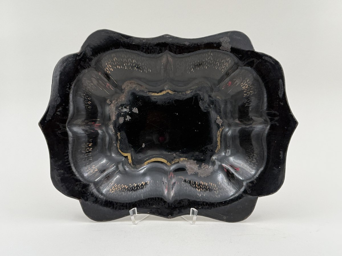 Svartlackerad brödkorg av plåt. Konturerad form med spår av förgylld dekor invändigt.