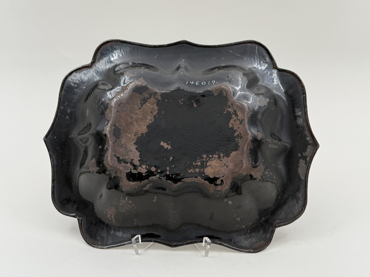 Svartlackerad brödkorg av plåt. Konturerad form med spår av förgylld dekor invändigt.