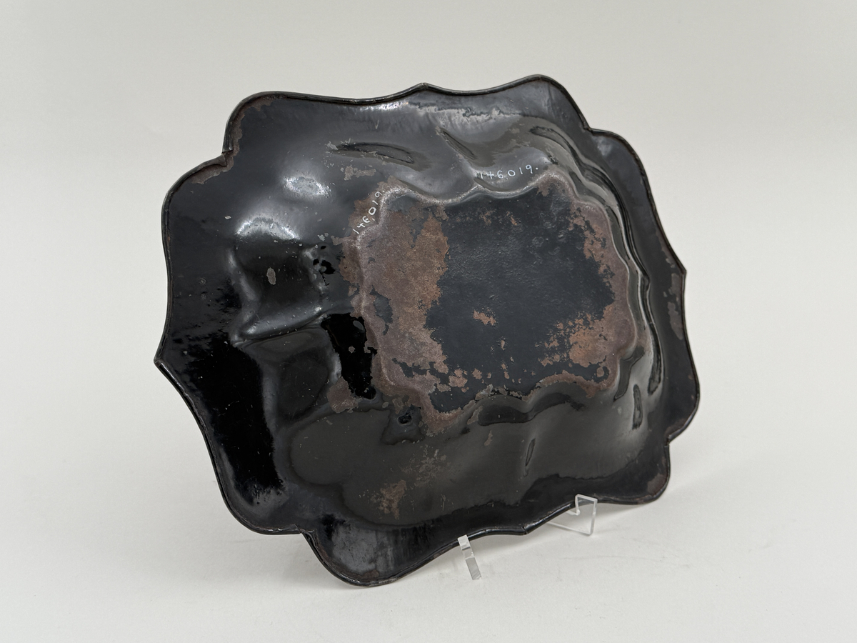 Svartlackerad brödkorg av plåt. Konturerad form med spår av förgylld dekor invändigt.