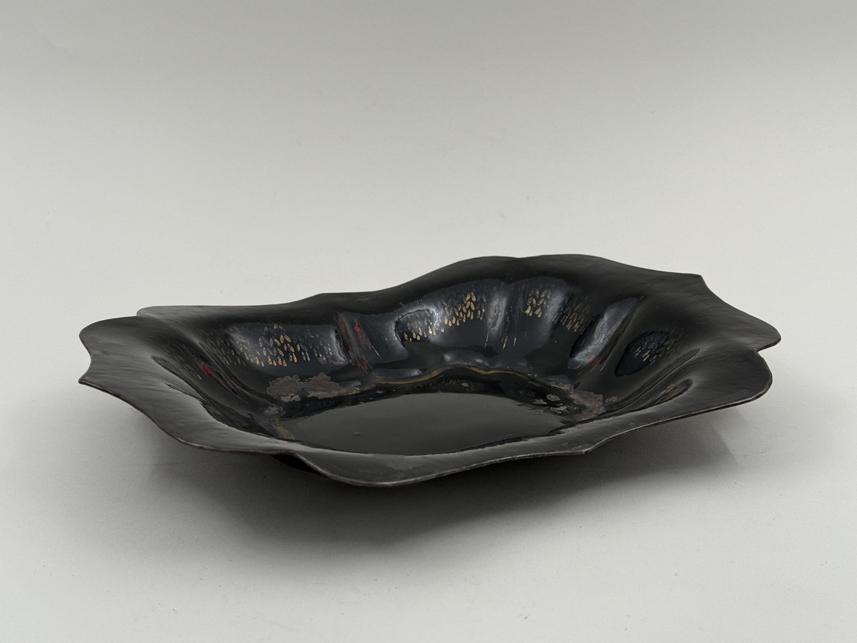 Svartlackerad brödkorg av plåt. Konturerad form med spår av förgylld dekor invändigt.