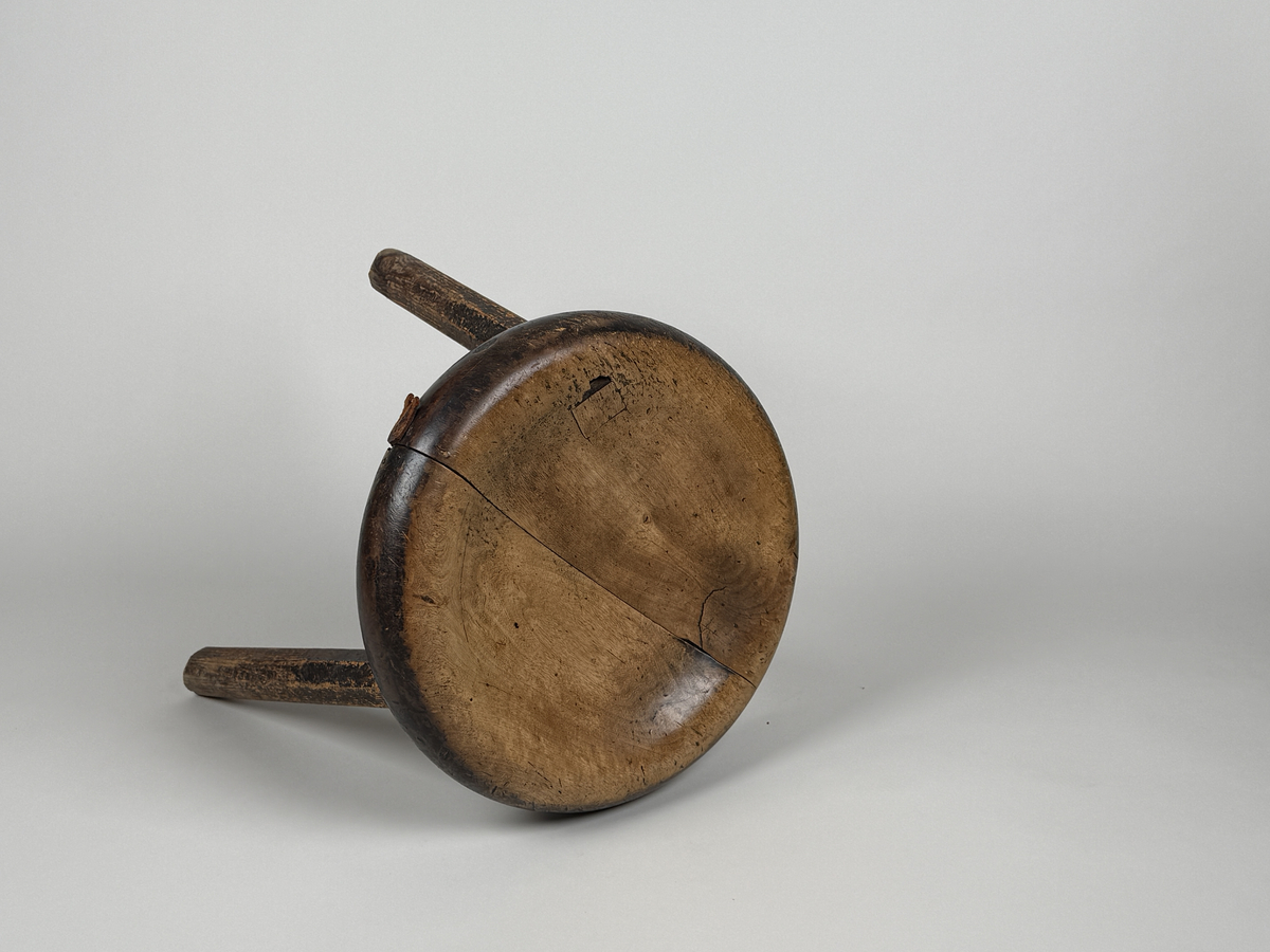 Pall med skålad sits av björk, åttkantiga ben av furu. Benen med ojämn längd så pallen lutar. Sitsen sprucken samt lagad med läderbitar och nubb. 